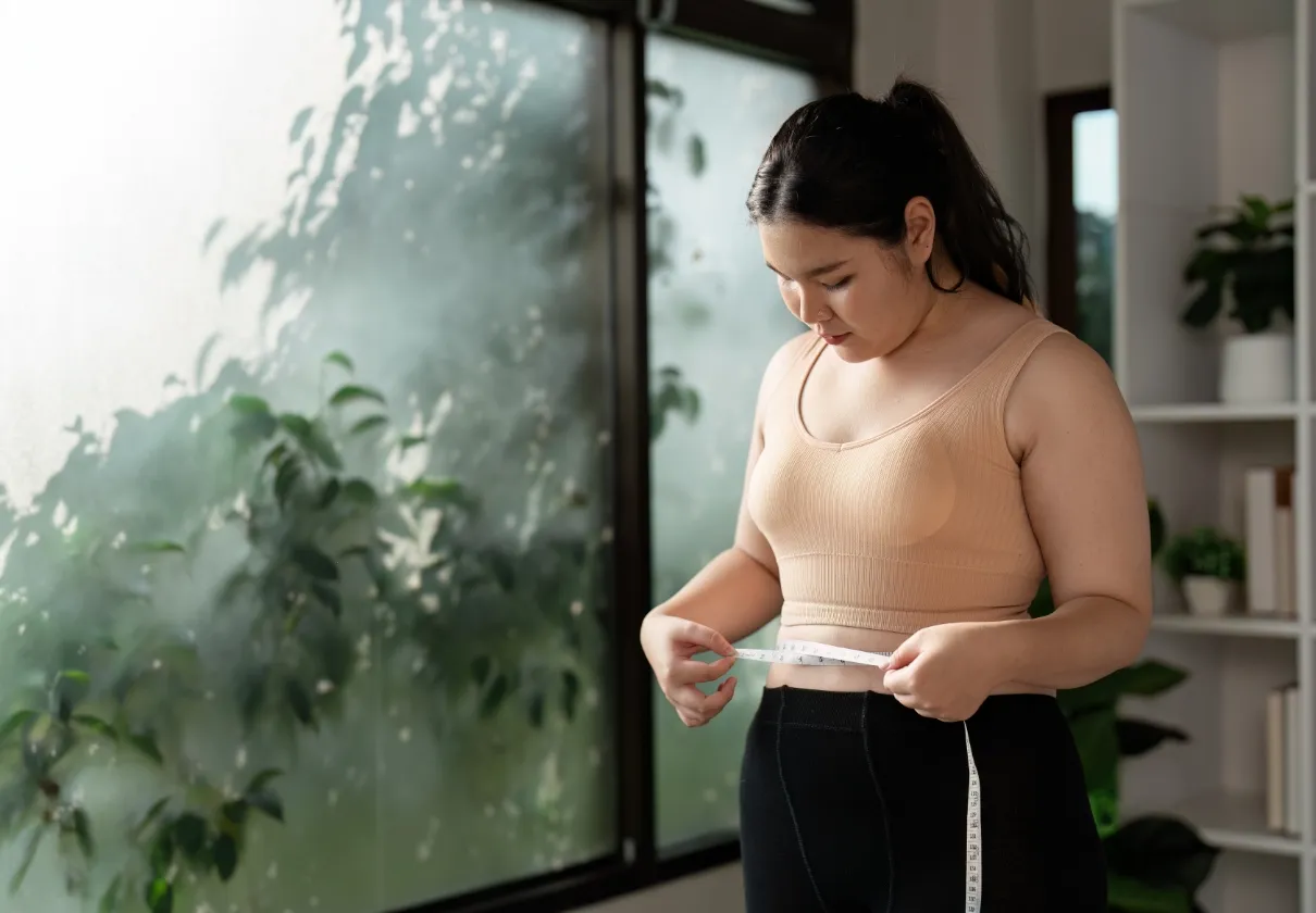 confident woman measuring waist in modern home gym utc